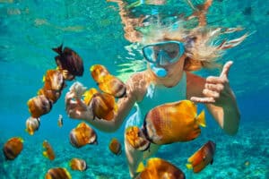 Happy family - girl in snorkeling mask dive underwater with tropical fishes in coral reef sea pool. Travel lifestyle, water sport outdoor adventure, swimming lessons on summer beach holiday with kids