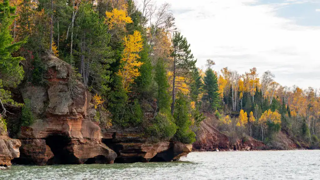 Apostle Islands mainland sea caves along the Bayfield Peninsula with autumn trees and rocky cliffs above the water.