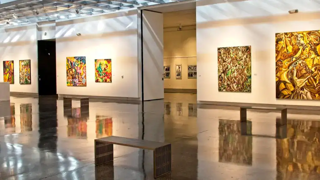 Art gallery interior with colorful abstract paintings displayed on white walls and reflective polished floors.