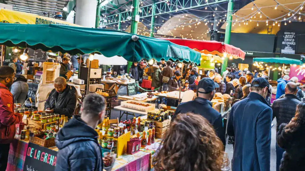 Crowds exploring food stalls at a vibrant outdoor market under colorful awnings and string lights