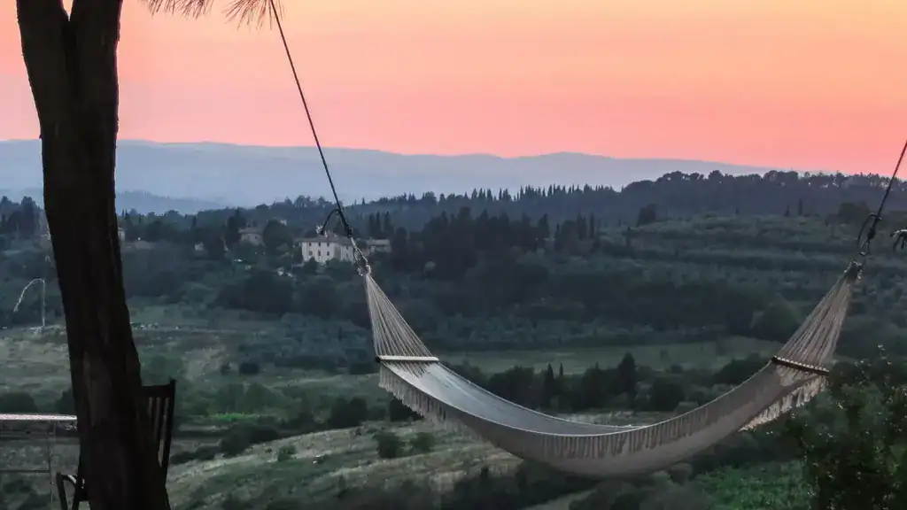 Hammock tied between two trees overlooking rolling hills and a colorful sunset in the Tuscan countryside.