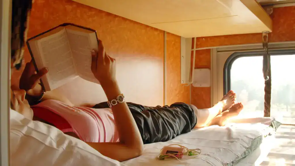 Traveler relaxing on a night train bunk while reading a book