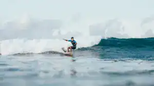 young sportsman in wetsuit riding waves on surfboard on sunny